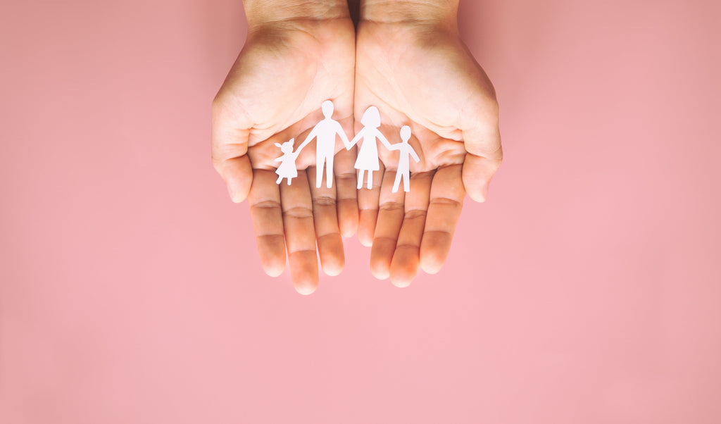 Hand holding family paper cut on pink background showing parents’ autism support for world autism day.