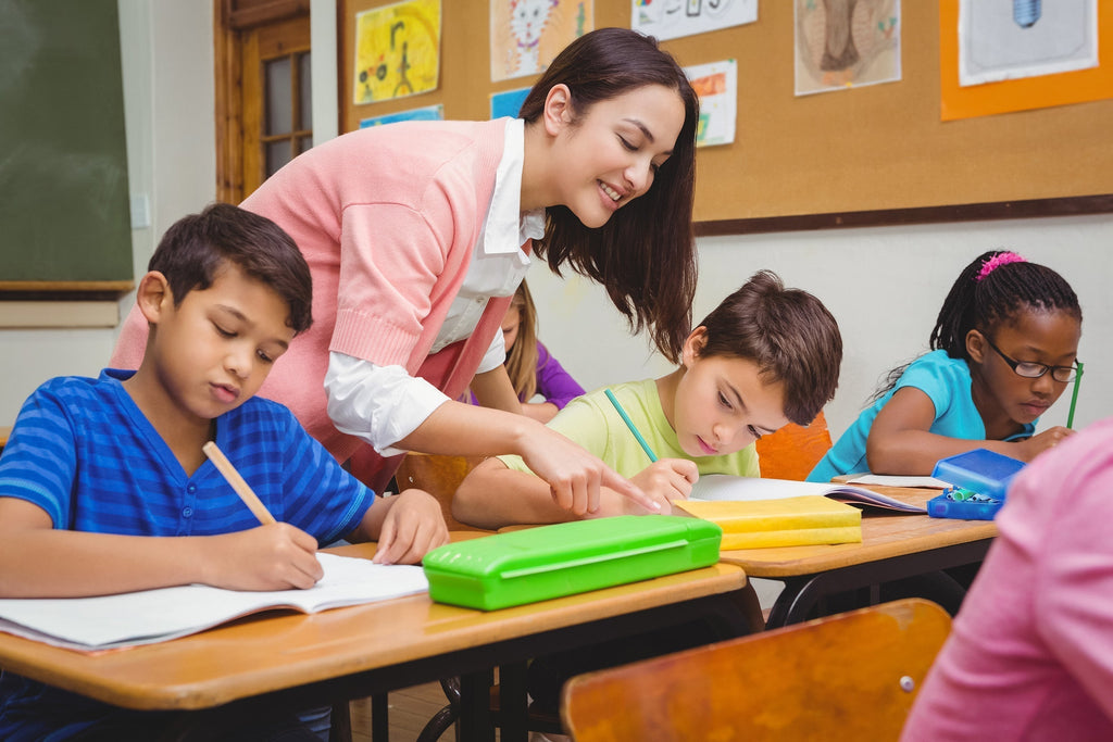 Teacher leaning over an autistic students’ desk to help them with work.